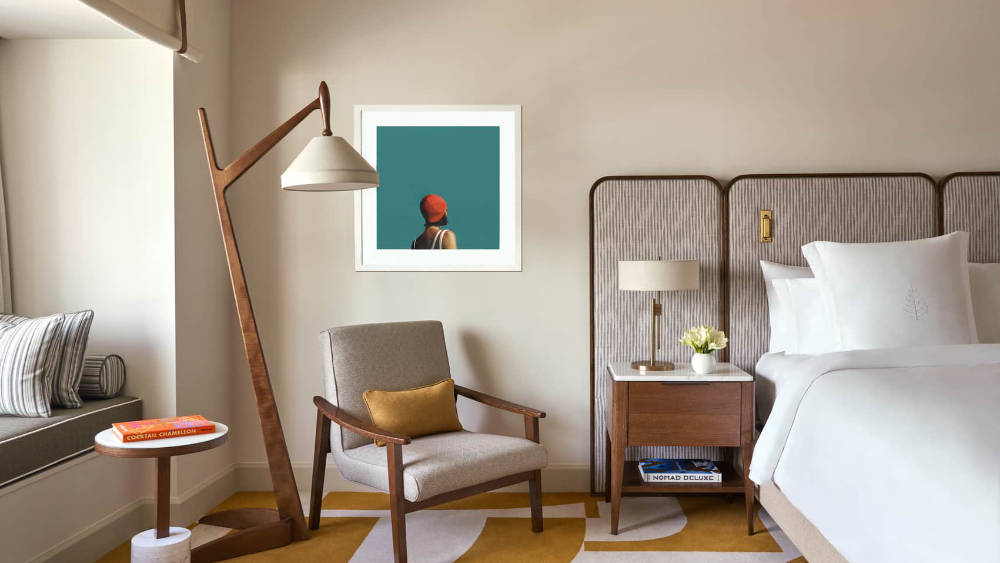 Four Seasons Miami guest room with crisp white bedding, a gray armchair, sculptural wood floor lamp, and colorful contemporary artwork.