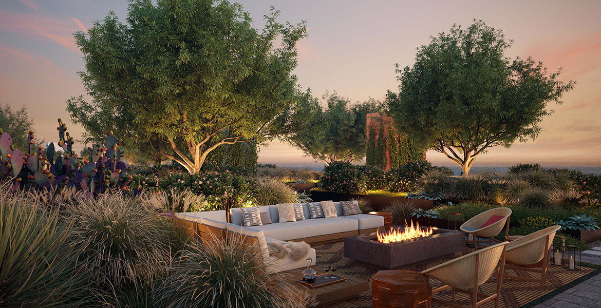 500 Broadway rooftop amenity terrace with lounge seating around a rectangular fire pit, surrounded by lush grasses, trees, and desert plants at sunset.