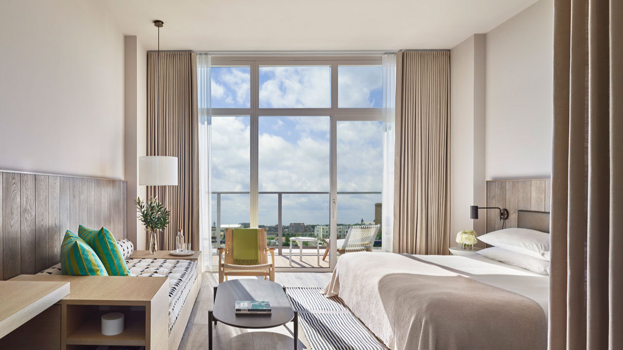 Asbury Ocean Club guest room with a white bed, built-in daybed, colorful pillows, and floor-to-ceiling doors opening to a balcony.