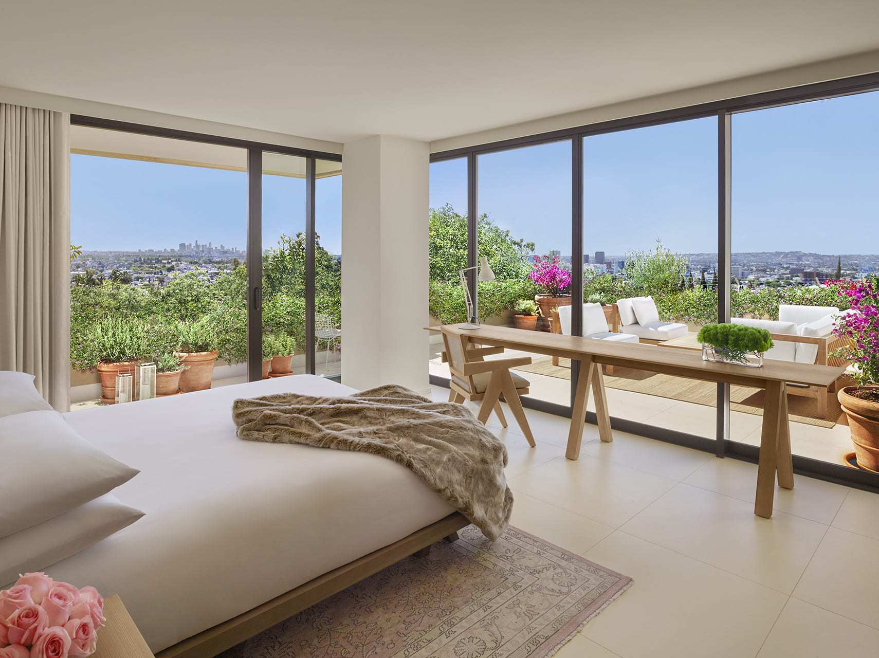 West Hollywood EDITION guest room with floor-to-ceiling glass walls, a terrace filled with potted plants, and panoramic Los Angeles views.