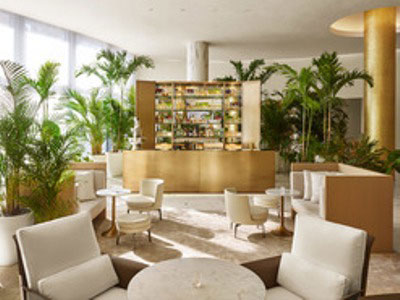 Miami Beach EDITION lobby lounge with white seating, round tables, a central bar, and abundant indoor palm trees.