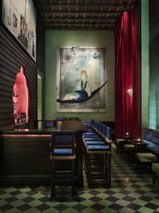 Gramercy Park Hotel lounge with deep green walls, red velvet curtains, blue banquette seating, checkerboard floor, and large contemporary artwork.