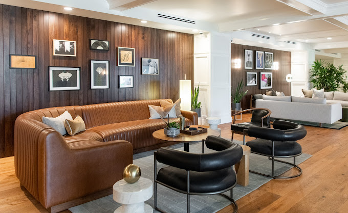 Hutton Hotel lobby with a long brown leather banquette, black lounge chairs, wood-paneled gallery wall, and framed artwork.