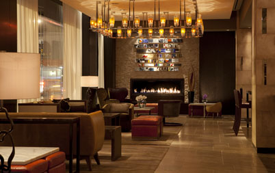 InterContinental Times Square lounge with a linear pendant chandelier, fireplace, upholstered seating, and warm amber lighting.