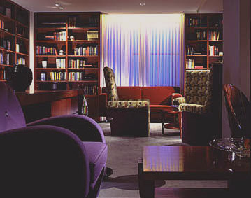 Loews Philadelphia Hotel lounge with dark bookshelves, purple and patterned armchairs, and a softly illuminated central curtain.