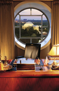 Mandarin Oriental desk beneath a large circular window, with twin lamps, small American flags, and a city landmark view beyond.
