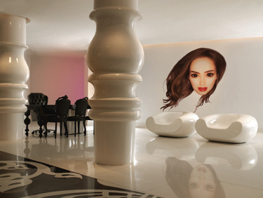 Mondrian South Beach lobby with oversized white columns, sculptural seating, a black grand piano, and a large portrait reflected on the glossy floor.