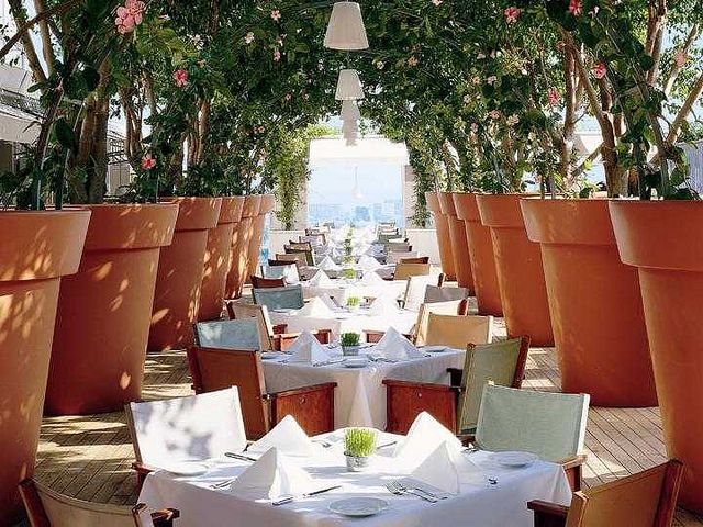 Mondrian West Hollywood terrace restaurant with white-tablecloth tables arranged between oversized terracotta planters and flowering trees.