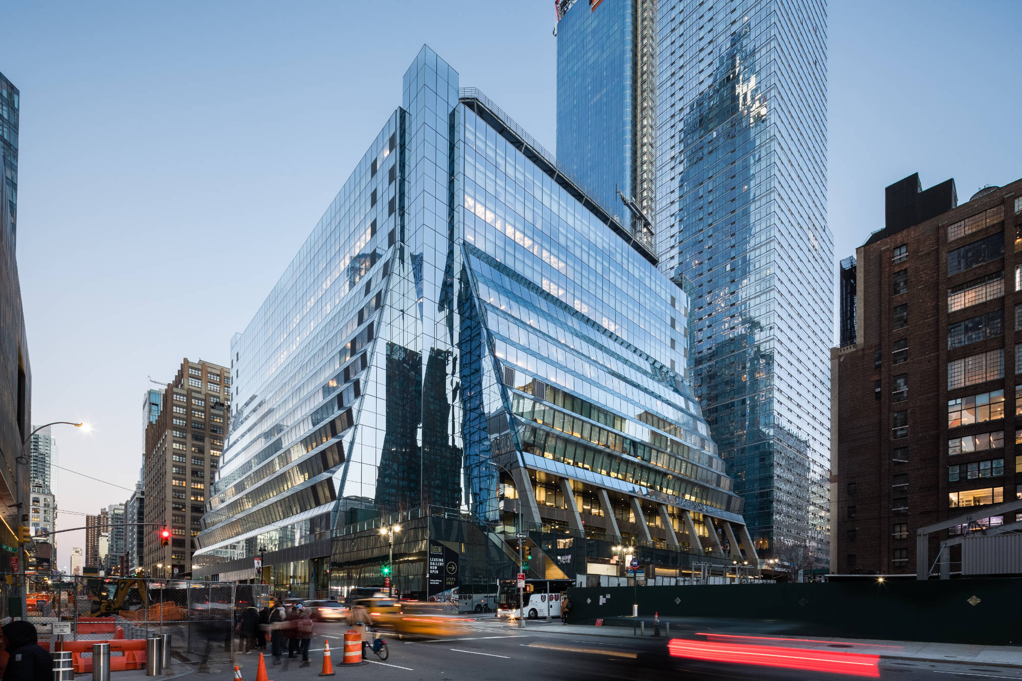 Noom Headquarters exterior with a faceted glass office building rising above a busy city street, with taller glass towers behind it.