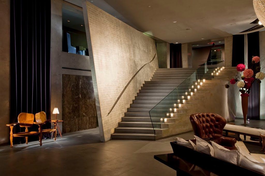 Paramount Hotel lobby with a broad illuminated staircase, glass railing, leather seating, and a tall floral arrangement.