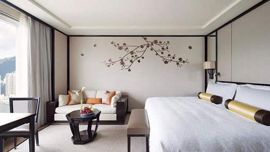 Peninsula Hong Kong guest room with a white bed, compact sofa sitting area, floral branch wall motif, and a city view.