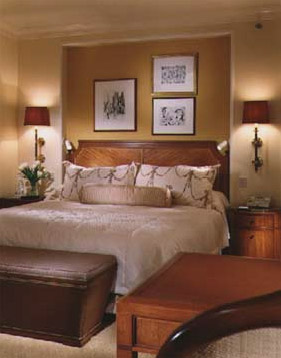 Peninsula Chicago guest room with a large cream bed, floral pillows, wood headboard, leather bench, and framed artwork.
