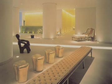 St. Martins Lane Hotel interior with a long tufted bench, metallic sculptural stools, a black figure-shaped chair, and soft yellow ambient lighting.
