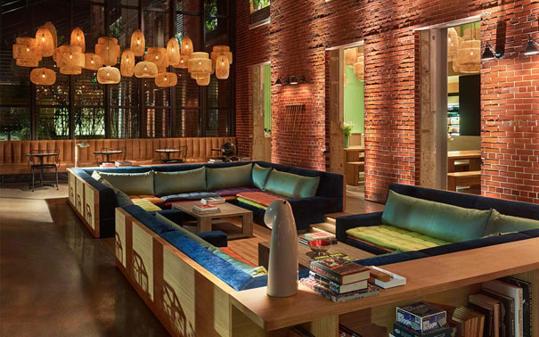 The Asbury Hotel lounge with exposed brick walls, deep blue and green sectional seating, bookshelves, and clustered woven pendant lights.