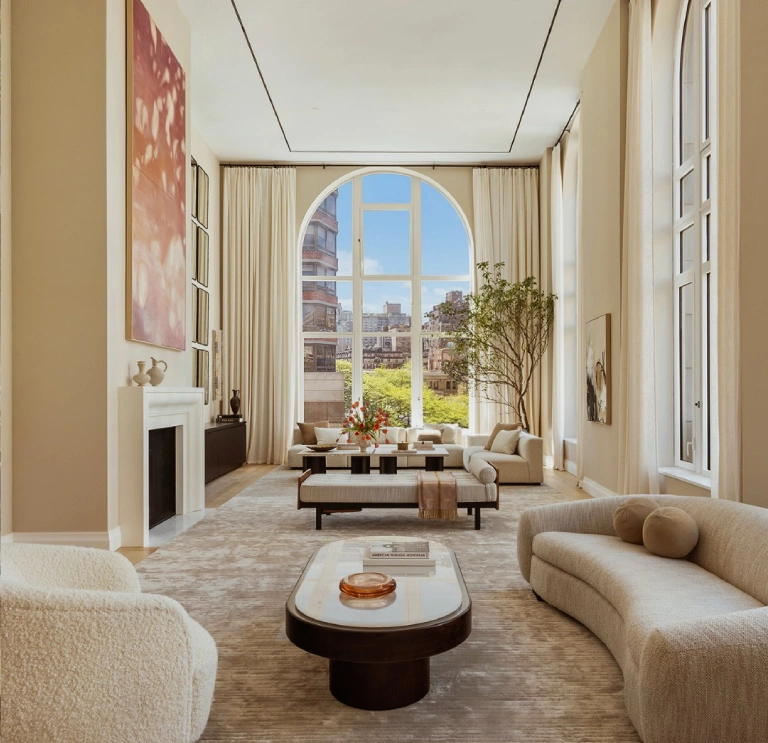 Bright Henry Residences living room with cream seating, a fireplace, and a floor-to-ceiling arched window overlooking the city.