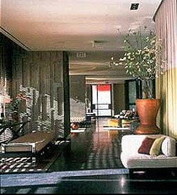 W Hotel lounge with a long window-side bench, white sofa, tall potted plant, and glossy dark flooring.